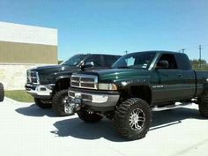 two trucks parked in front of a building with large tires on the back of them