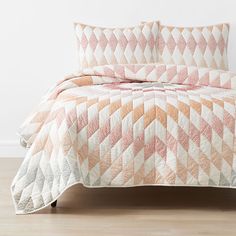 a bed with a pink and white quilt on top of it next to a wooden floor