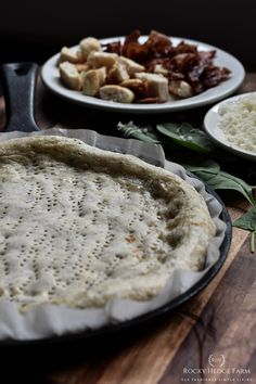 an uncooked pizza sitting on top of a wooden table next to other food