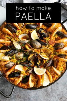 paella in a skillet with clams and lemon wedges on the side