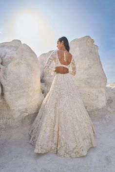 a woman in a white wedding dress standing next to large rocks and looking off into the distance