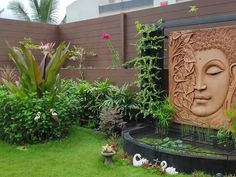 an outdoor garden with plants and statues in the center, along side a wall that has a buddha face on it