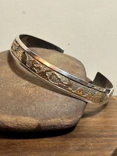 This is a gorgeous, vintage, genuine, handmade Navajo 12K yellow gold filled and sterling silver Storyteller cuff bracelet that was hand-made by renowned Navajo jewelry artisans, husband and wife Tom & Sylvia Kee. The bracelet features stamped 12K yellow gold-filled Storyteller symbols on the center of the face, including people, mountains, symbols and more. The bracelet is iconic of the Kee's workmanship and is well-made and stunning, as you would expect. The inner circumference of the bracelet is about 6 3/4 inches including its opening. The gap opening is about 1". The bracelet measures about 2 3/8" by 2". It has some bend to accommodate a larger or smaller wrist but best to let a jeweler adjust it because of its intricate workmanship. The bracelet is about 3/8" in width all around. It Stamped 925 Silver Bangle For Anniversary, Adjustable Etched Sterling Silver Bracelet For Anniversary, Etched Sterling Silver Bracelet As Gift, Etched Sterling Silver Bracelet Gift, Traditional Engraved Sterling Silver Bracelet For Anniversary, Antique 14k Stamped Bangle As Gift, Unique Gold Sterling Silver Cuff Bracelet, Adjustable Hallmarked Sterling Silver Bracelet For Ceremonial Occasions, Antique Stamped 925 Bracelets For Anniversary