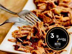 a white plate topped with shredded meat next to a fork and knife on top of a wooden table