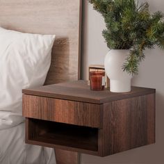 a nightstand with a plant on it next to a bed