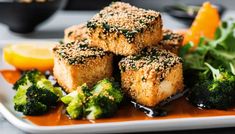 several pieces of tofu on a plate with broccoli and orange wedges