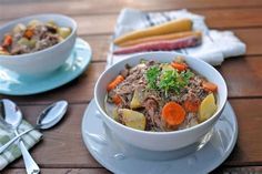 a bowl of stew with carrots, potatoes and celery on a wooden table