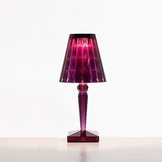 a purple lamp sitting on top of a table next to a white wall and floor