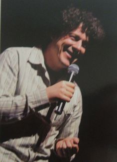 a man holding a microphone in his right hand and smiling at the camera while wearing a striped shirt