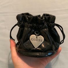 a hand holding a small black purse with a heart tag on it's side