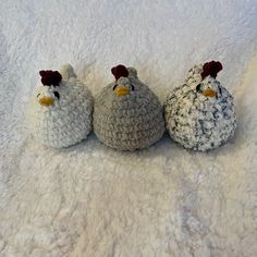 three crocheted chickens sitting next to each other on a white surface with one chicken looking at the camera