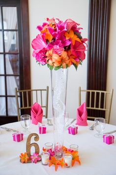 a tall vase filled with pink and orange flowers on top of a white table cloth