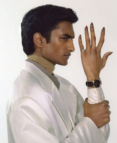 a man in a white suit holding his hand up to the side with both hands