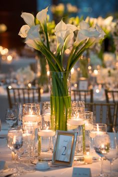 a vase filled with white flowers sitting on top of a table covered in glasses and candles