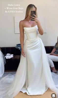 a woman in a white dress taking a selfie with her cell phone while wearing a wedding gown