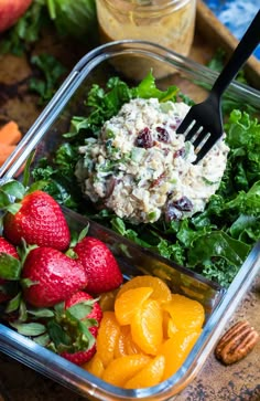 a plastic container filled with salad and fruit on top of a wooden table next to nuts