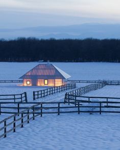 a barn in the middle of a snow covered field with a lit up window at night