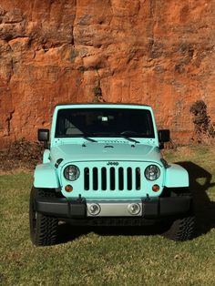 a light blue jeep parked in front of a large rock formation with grass and rocks behind it