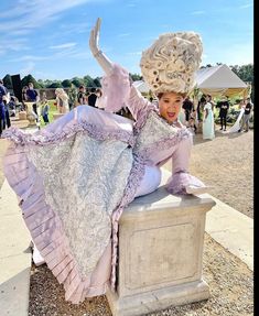 a woman sitting on top of a cement block in a dress and hat with her legs spread out