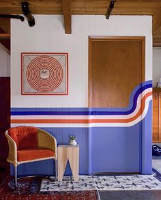 an orange chair sitting in front of a blue and white wall with a painting on it