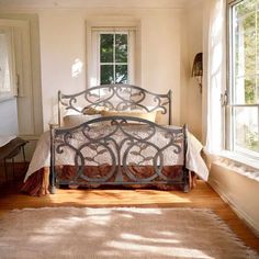 a bed sitting in a bedroom next to a window with sunlight coming through the windows