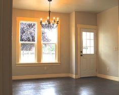 an empty room with two windows and a chandelier hanging from the light fixture