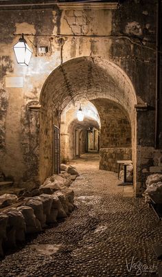 an alley way with stone walls and cobblestone walkway leading into the light at the end