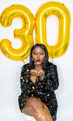 a woman sitting on top of a white chair next to a number 30 balloon in the air