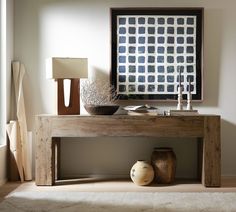 a wooden table with vases on it in front of a wall mounted art piece