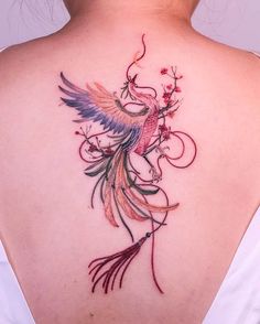 the back of a woman's neck with a bird and flowers tattoo on it