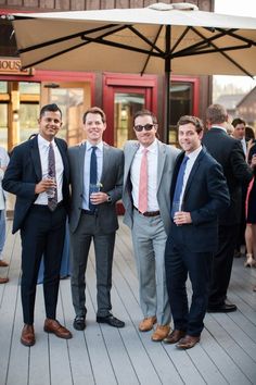 three men in suits and ties are posing for a photo on a deck with other people