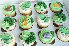 twelve cupcakes decorated with green frosting and animals on them are sitting in a box