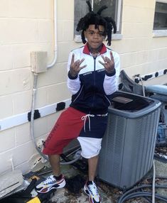 a man with dreadlocks sitting in front of an air conditioner and holding his hands up