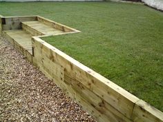 wooden steps leading up to the grass in a garden area with gravel and stones on the ground