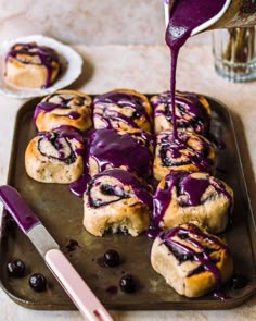 blueberry rolls are being drizzled with icing on a baking sheet