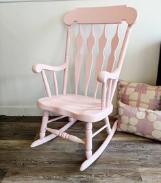 a pink rocking chair sitting on top of a hard wood floor next to a pillow