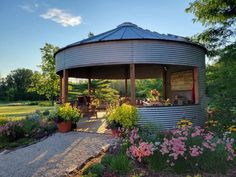 a round metal structure sitting in the middle of a garden with flowers and plants around it