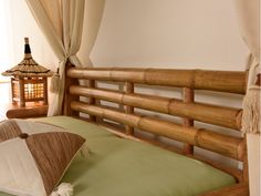 a bamboo bed frame with green pillows and white curtains in front of a small window