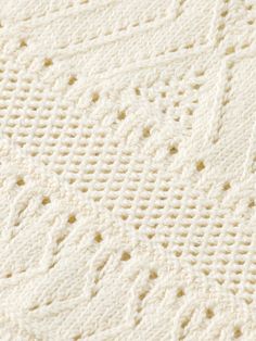 a white crocheted blanket is laying on top of a tablecloth that has holes in it