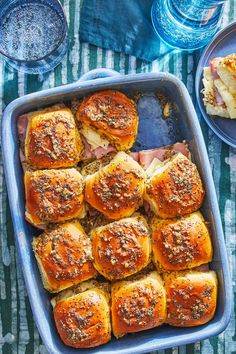 a blue dish filled with meat and cheese sliders on top of a green table cloth