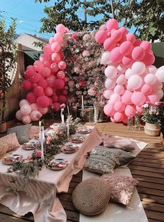 a table set up with pink balloons and plates on top of it, surrounded by greenery