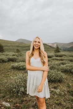 a woman standing in a field with her arms crossed looking at the camera and smiling