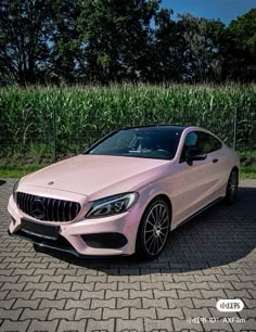 a pink mercedes cla is parked in front of some corn stalks on a brick road