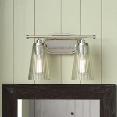 two light bathroom fixture with clear glass shades on the wall and mirror in front of it