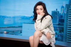 a woman sitting on top of a window sill in front of a cityscape