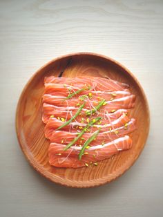 raw salmon on a wooden plate with sprigs and seasoning in it, ready to be eaten