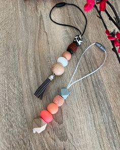 three necklaces with different colors and shapes on a wooden table next to an orange flower