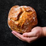 a person holding a loaf of bread in their hand on a black surface with white writing