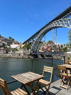 an outdoor table and chairs on a deck overlooking the water with a bridge in the background