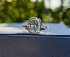 an oval cut diamond ring sitting on top of a blue tablecloth with trees in the background